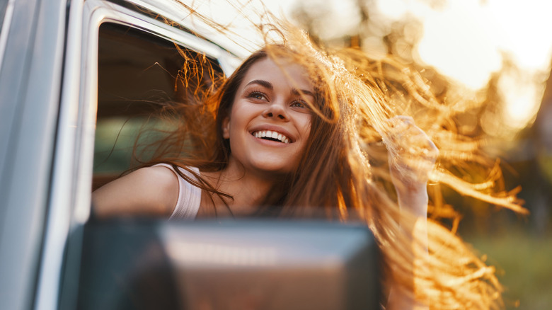 Jeune femme avec la tête hors de la fenêtre de la voiture, souriant tandis que les cheveux soufflent dans le vent