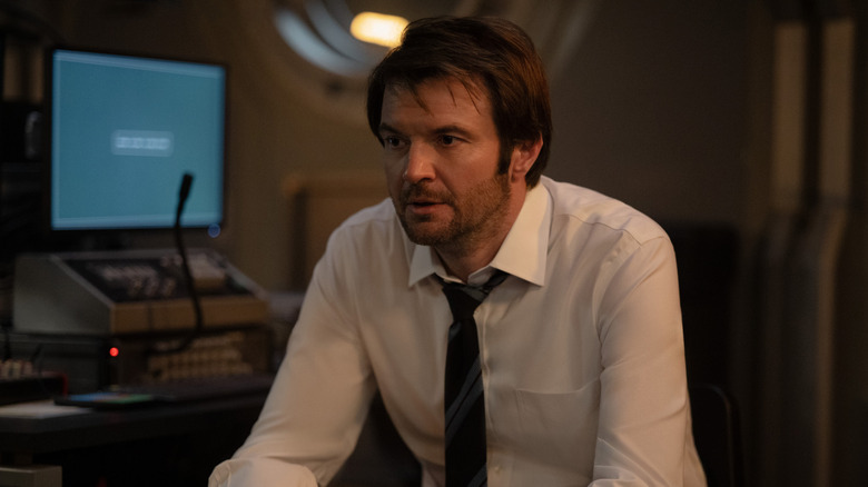 Costa Ronin dans le rôle de Leonid Polivanov, assis près d'un écran d'ordinateur, vêtu d'une chemise et d'une cravate, l'air échevelé dans For All Mankind