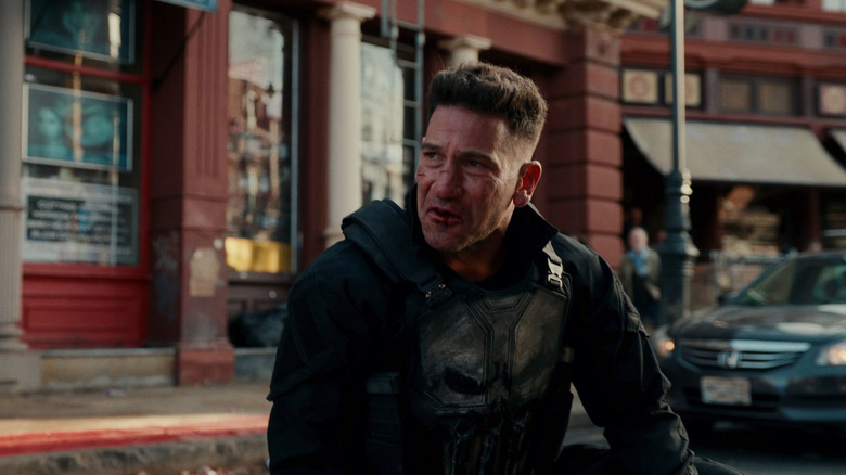 Jon Bernthal dans le rôle de Frank Castle portant sa tenue Punisher et agenouillé dans une rue animée dans Spider-Man : Brand New Day