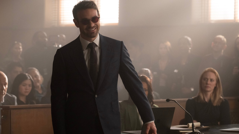 Charlie Cox dans le rôle de Matt Murdock portant un costume et une cravate et debout dans une salle d'audience devant Deborah Ann Woll dans le rôle de Karen Page dans Daredevil : Born Again