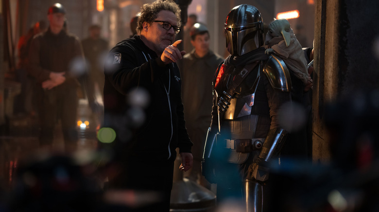 Le réalisateur Jon Favreau fait signe à Pedro Pascal dans le rôle de Din Djarin dans une rue animée remplie de acteurs et d'équipes sur le tournage de Star Wars : The Mandalorian et Grogu