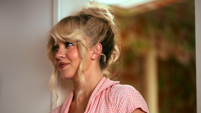 Cassie dans une chemise à carreaux vichy rose, les cheveux relevés, souriant à quelqu'un sur Euphoria