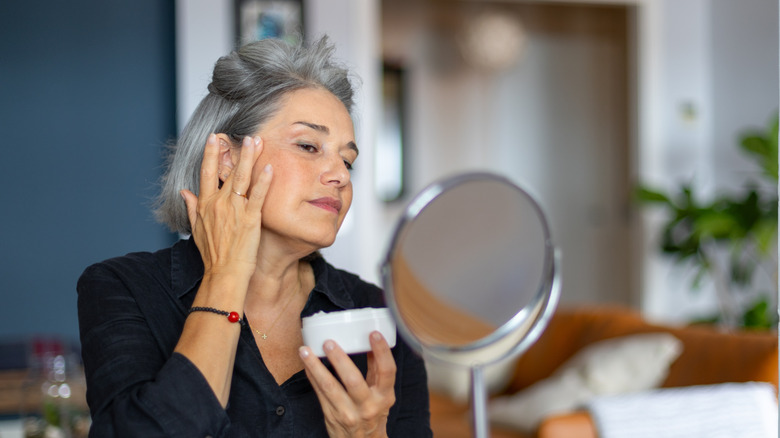 Une femme mûre appliquant un produit de soin sur son visage