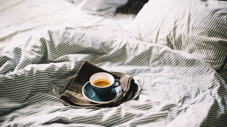 Une tasse de café posée sur un lit défait.