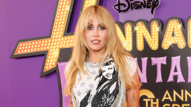 Miley Cyrus pose vêtue d'un T-shirt blanc orné et d'un collier en cristal