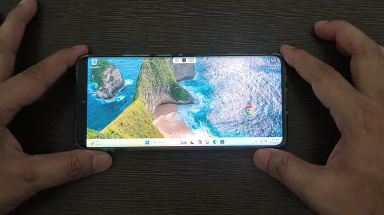 Une personne tenant un téléphone Android affichant un bureau Windows 11