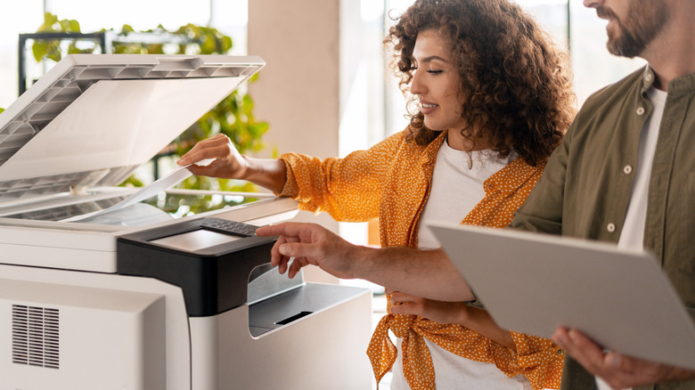 Une personne met du papier dans une imprimante scanner pendant que quelqu'un d'autre utilise sa console