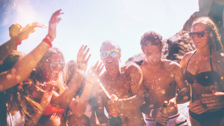jeunes adultes faisant éclater du champagne à la plage pour faire la fête