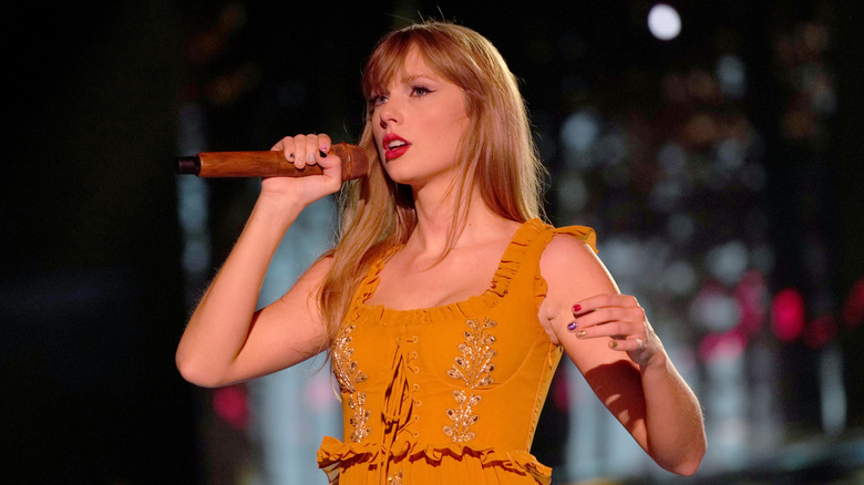 Taylor Swift porte une robe orange lorsqu'elle chante sur scène et regarde le public avec nostalgie.