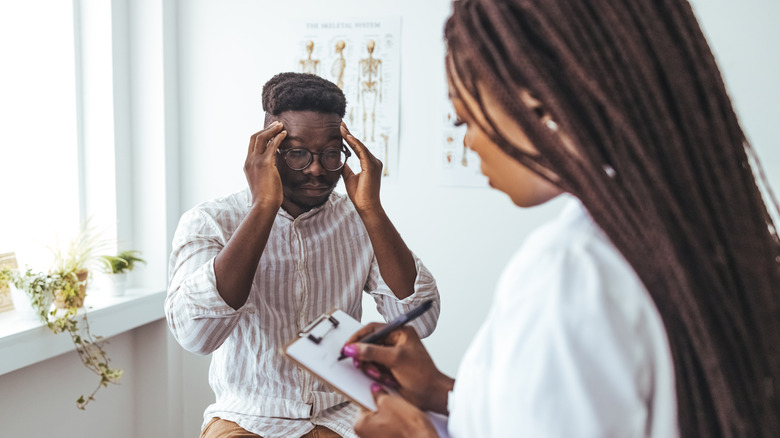 Homme avec les mains sur les tempes tout en parlant avec un médecin