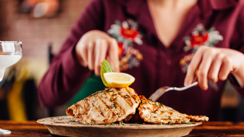 Personne coupant une poitrine de poulet cuite dans une assiette