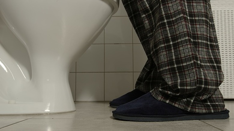 Vue des toilettes depuis le sol avec une personne en pantalon de pyjama et pantoufles debout devant