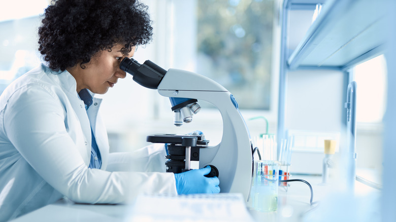Femme en blouse regardant un microscope