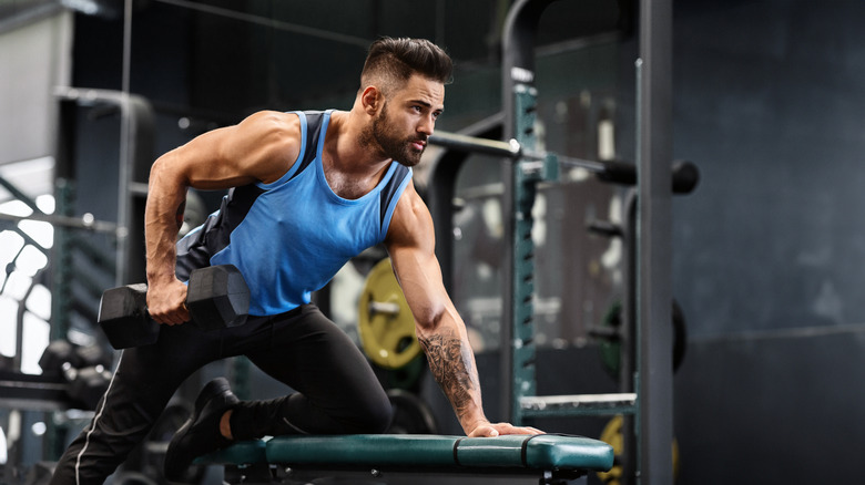 homme dans une salle de sport faisant des rangées d'haltères à un bras sur un banc de musculation