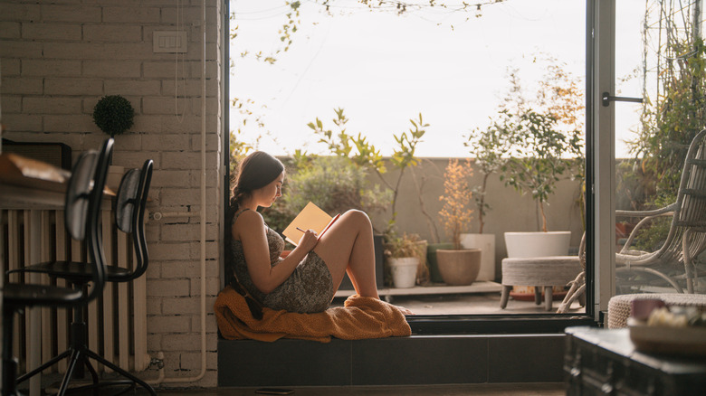 Une jeune femme assise devant une fenêtre écrivant dans un journal