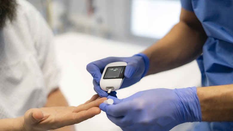 Un médecin portant des gants bleus mesure le taux de sucre dans le sang d'une femme avec un glucomètre