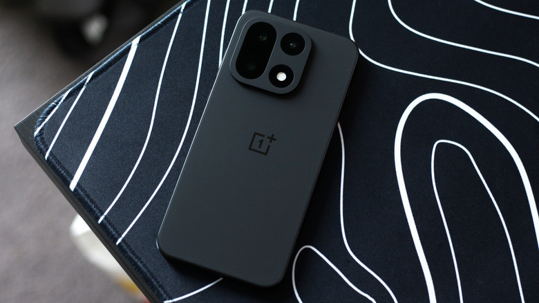 OnePlus 15 noir sur un tapis de souris avec un motif abstrait blanc et noir.