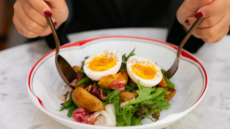 Personne mangeant une salade avec un œuf à la coque