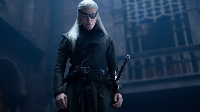 Ewan Mitchell dans le rôle d'Aemond Targaryen portant un cache-œil et se tenant au-dessus de quelqu'un de manière menaçante dans House of the Dragon