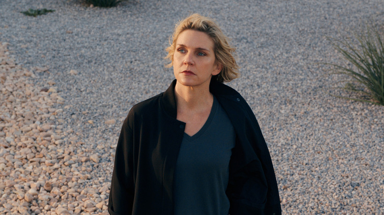 Rhea Seehorn dans le rôle de Carol Sturka debout sur un chemin de gravier par une journée venteuse à Pluribus