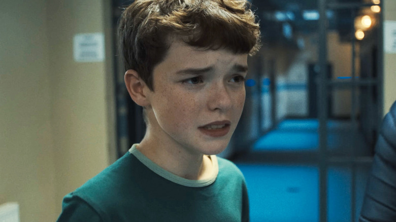 Jamie Miller d'Owen Cooper a l'air inquiet alors qu'il se tient dans le couloir d'un commissariat de police dans Adolescence
