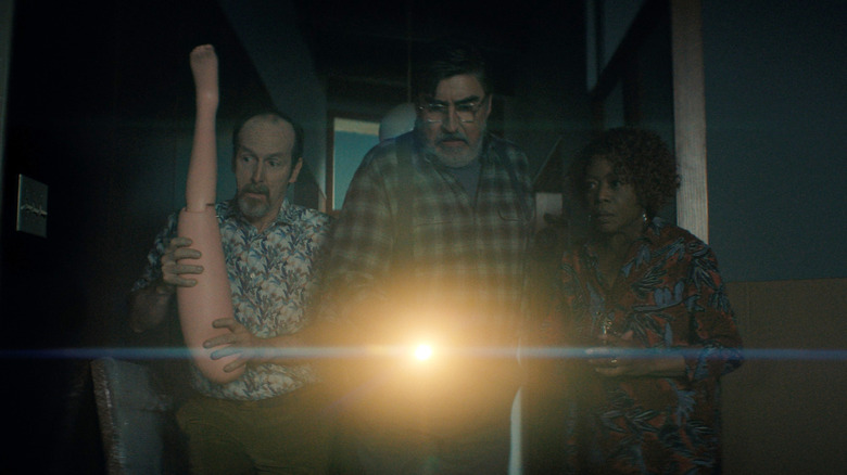 Denis O'Hare dans le rôle de Wally brandissant une jambe en plastique comme arme dans un couloir sombre à côté d'Alfred Molina dans le rôle de Sam et Alfre Woodard dans le rôle de Judy dans The Boroughs
