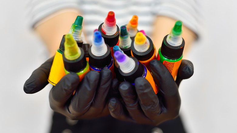 Mains gantées tenant différentes bouteilles de couleurs d'encre de tatouage