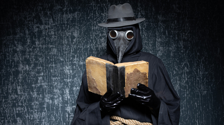 Un médecin de la peste debout devant un mur sombre en lisant un livre.