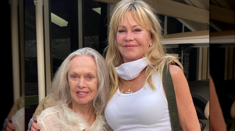 Melanie Griffith sourit avec son bras enroulé autour de sa mère Tippi Hedren, qui arbore des cheveux gris et un doux sourire.