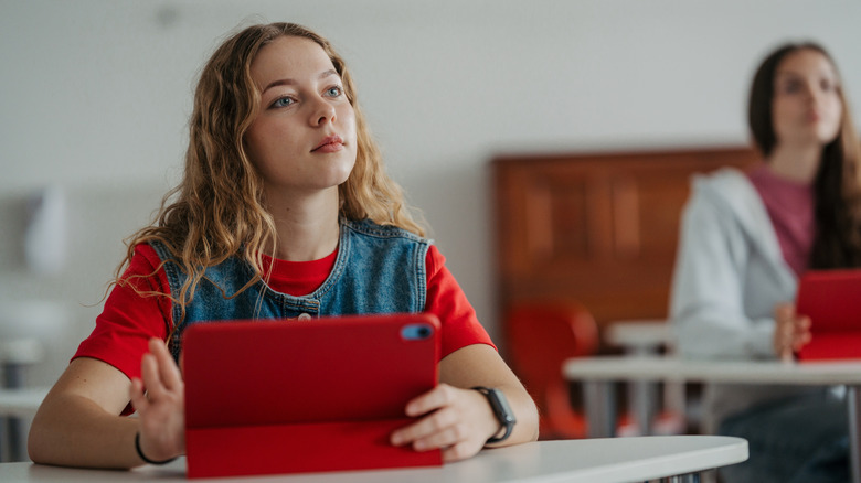 Un étudiant est assis à un bureau, tenant un iPad et regardant au-delà de la caméra.