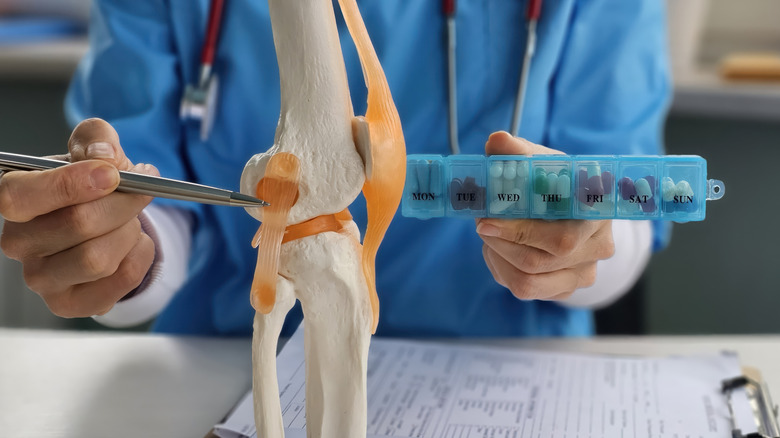 Médecin brandissant des médicaments tout en montrant le modèle du genou