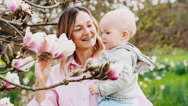 Mère tenant son bébé à côté d’un arbre en fleurs