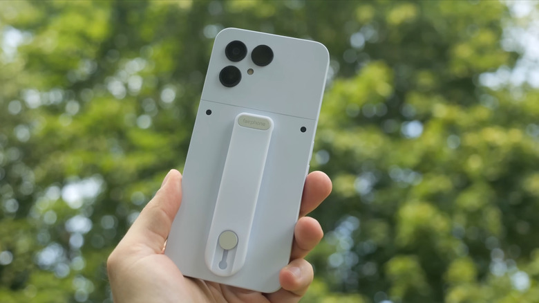 Une personne brandissant un Fairphone 6 blanc, des arbres en arrière-plan