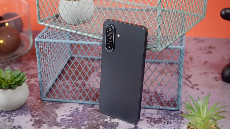 Le Samsung Galaxy A17 5G à côté de quelques pots de plantes et caisses métalliques, coloris noir