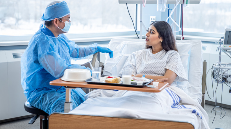 Médecin de sexe masculin parlant avec une femme dans un lit d'hôpital