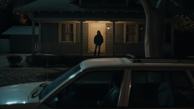 Michael Johnston dans le rôle de Bear assis dans sa voiture regardant Inde Navarrette alors que Nikki se tient d'un air menaçant sur le porche de sa maison dans Obsession