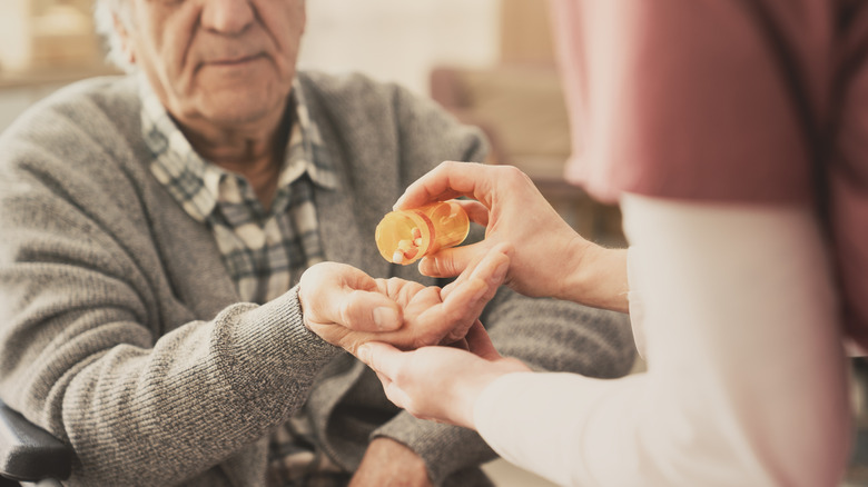 Un professionnel de la santé tend une pilule à un homme âgé.
