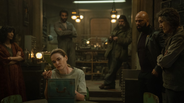 Rebecca Ferguson dans le rôle de Juliette Nichols assise dans une pièce et inspectant son insigne de shérif devant Avi Nash dans le rôle de Lukas Kyle, Rick Gomez dans le rôle de Patrick Kennedy, Common dans le rôle de Robert Sims et Harriet Walter dans le rôle de Martha Walker dans Silo