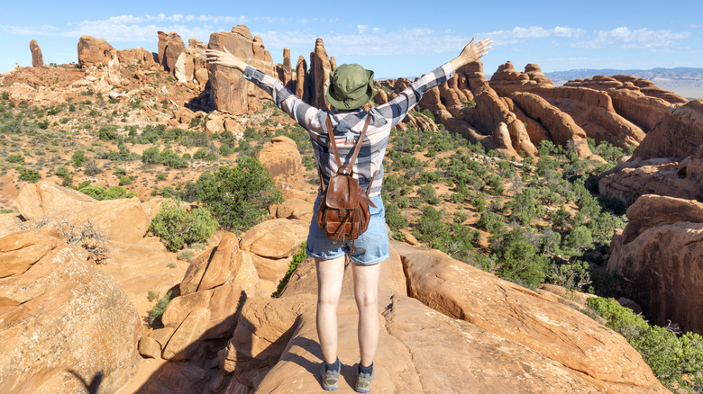 une femme debout avec les bras tendus surplombant le parc national des Arches dans l'Utah
