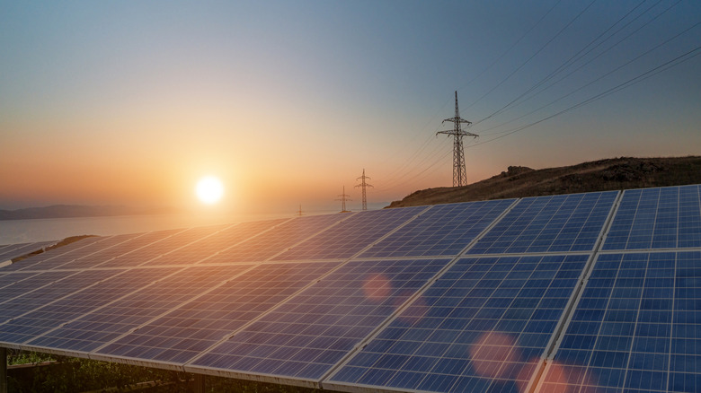 Panneaux solaires avec un soleil couchant et des lignes électriques en arrière-plan
