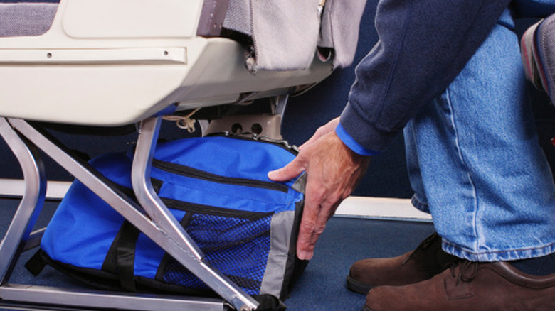 Mains rangeant un sac sous un siège d’avion.