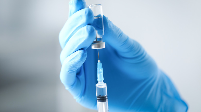 Mains gantées à l'aide d'une seringue pour prélever une solution d'un flacon en verre.