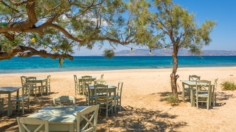 Tables et chaises sous un genévrier sur la plage de Plaka
