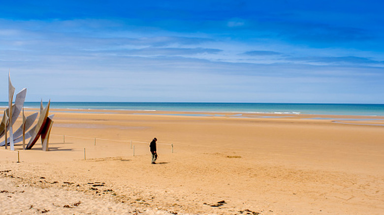 Un visiteur passe devant un monument sur le sable de la plage d'Omaha