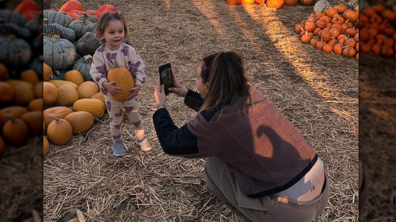 Kaley Cuoco s'accroupit pour prendre une photo de sa fille Matilda dans un champ de citrouilles.