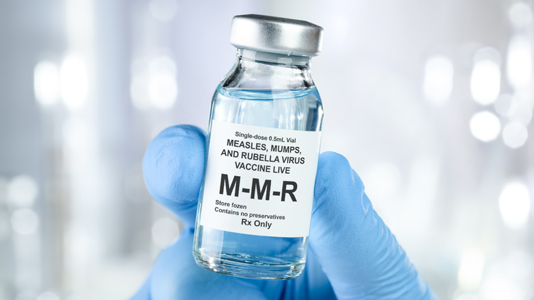 Une main gantée tenant un flacon de vaccin ROR