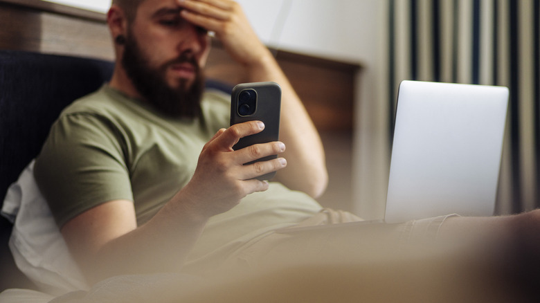 Homme tenant un smartphone au lit et semblant stressé