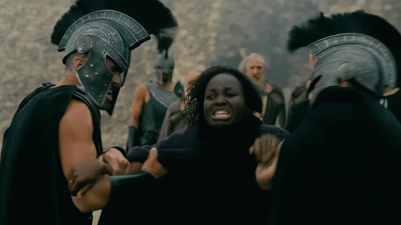 Lupita Nyong'o dans le rôle de Clytemnestre criant d'angoisse alors qu'elle est retenue par deux soldats dans L'Odyssée