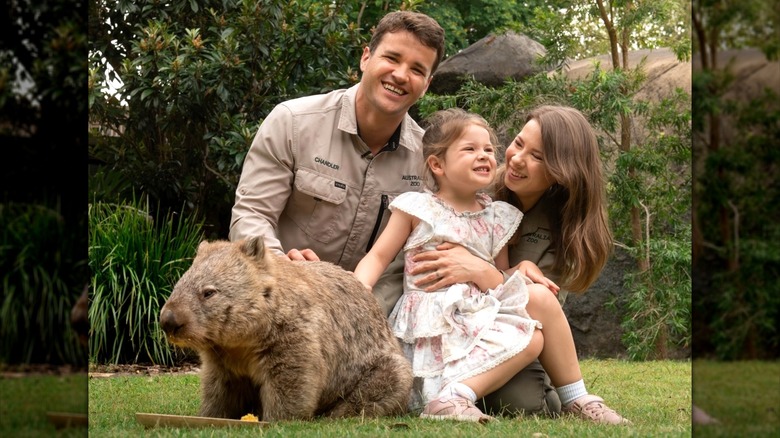 Bindi Irwin tient sa fille dans ses bras, posant à côté de son mari et d'un wombat.