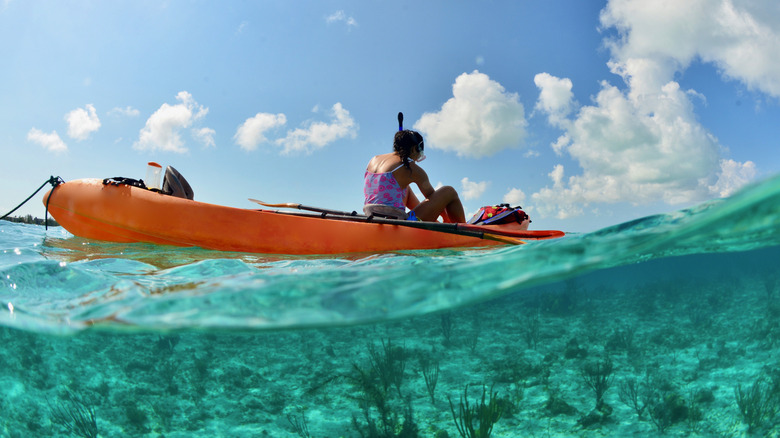 Une personne portant un équipement de plongée en apnée dans un kayak orange sur une eau vert clair aux Îles Turques et Caïques.